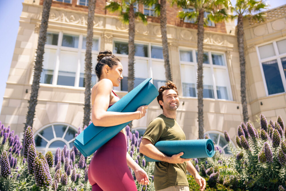 man and woman walking to the beach with yoga mats