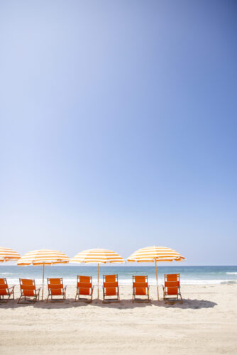 Row of orange beach chairs and striped umbrellas lined up by the ocean.