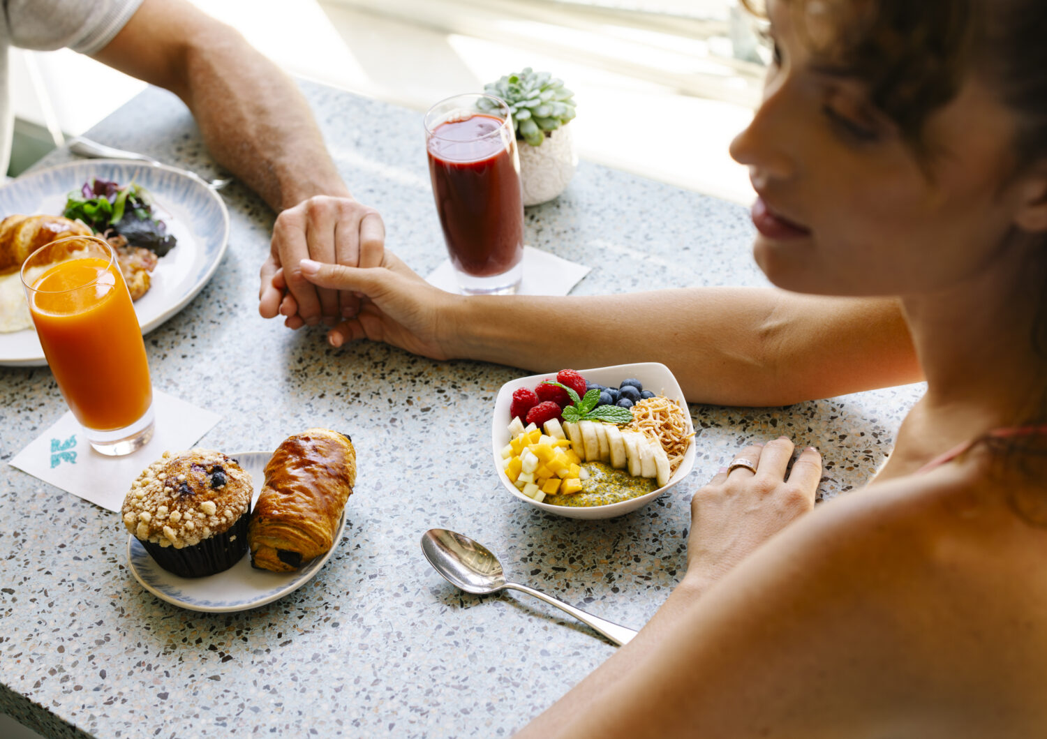 woman holding man's hand at a table with breakfast food in front of them
