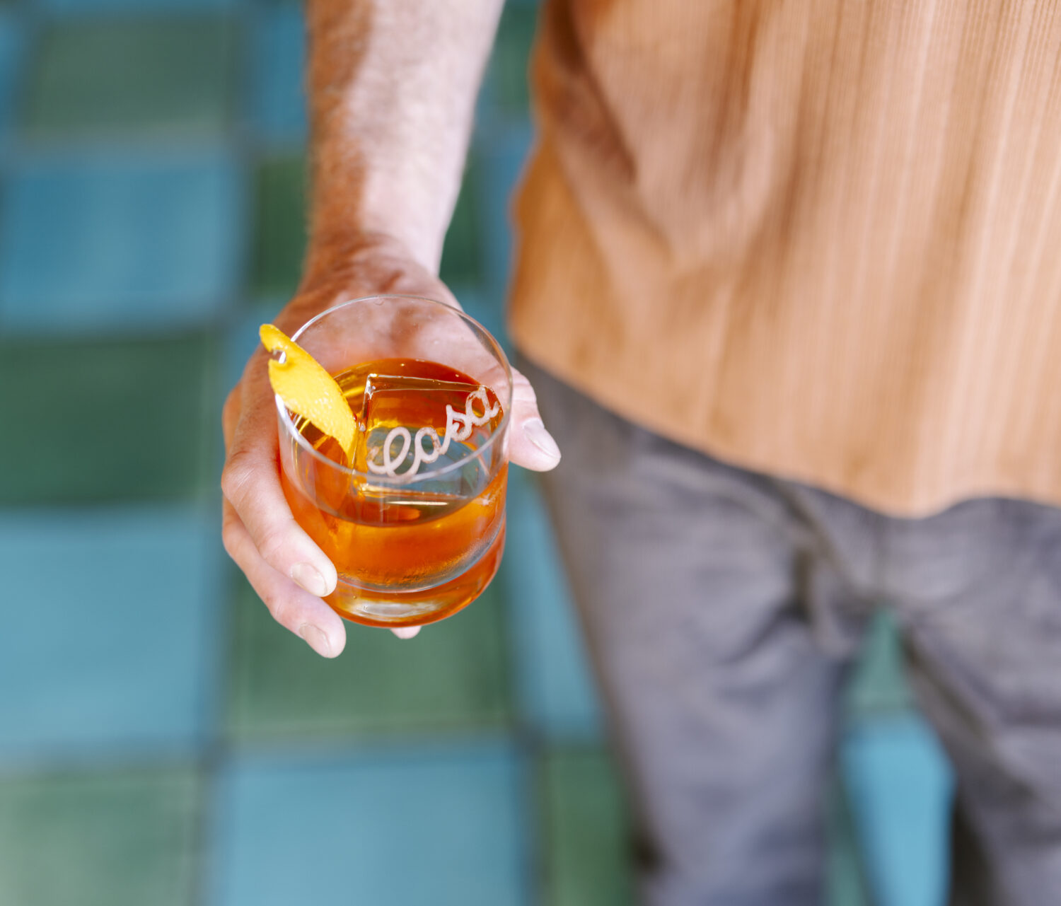 man holding a old fashioned cocktail with a custom carving of 'casa' on ice block