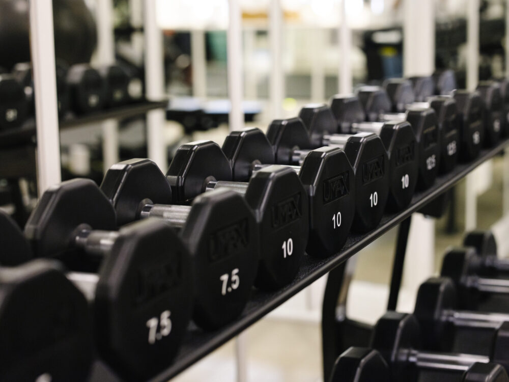 A rack of black hexagonal dumbbells in a gym, with a focus on the 10-pound dumbbells.