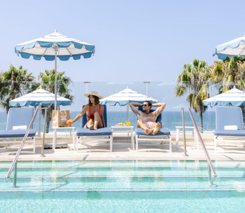 A couple relaxing on lounge chairs under umbrellas at Hotel Casa Del Mar pool, with an ocean view.