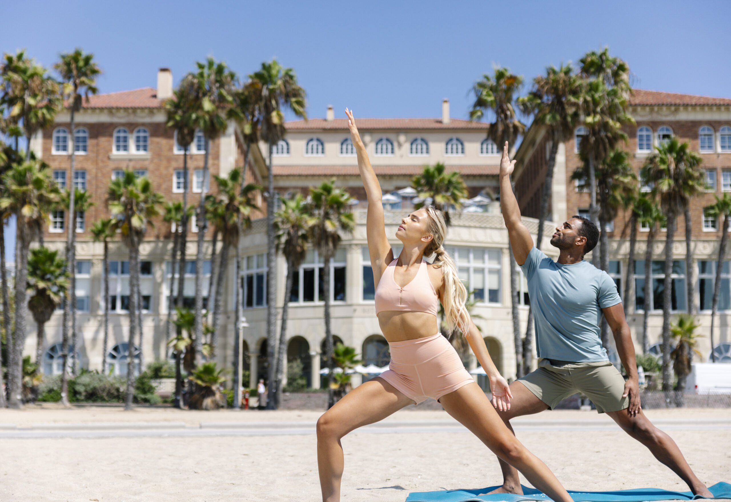 man and woman on the beach in a warrior 3 pose