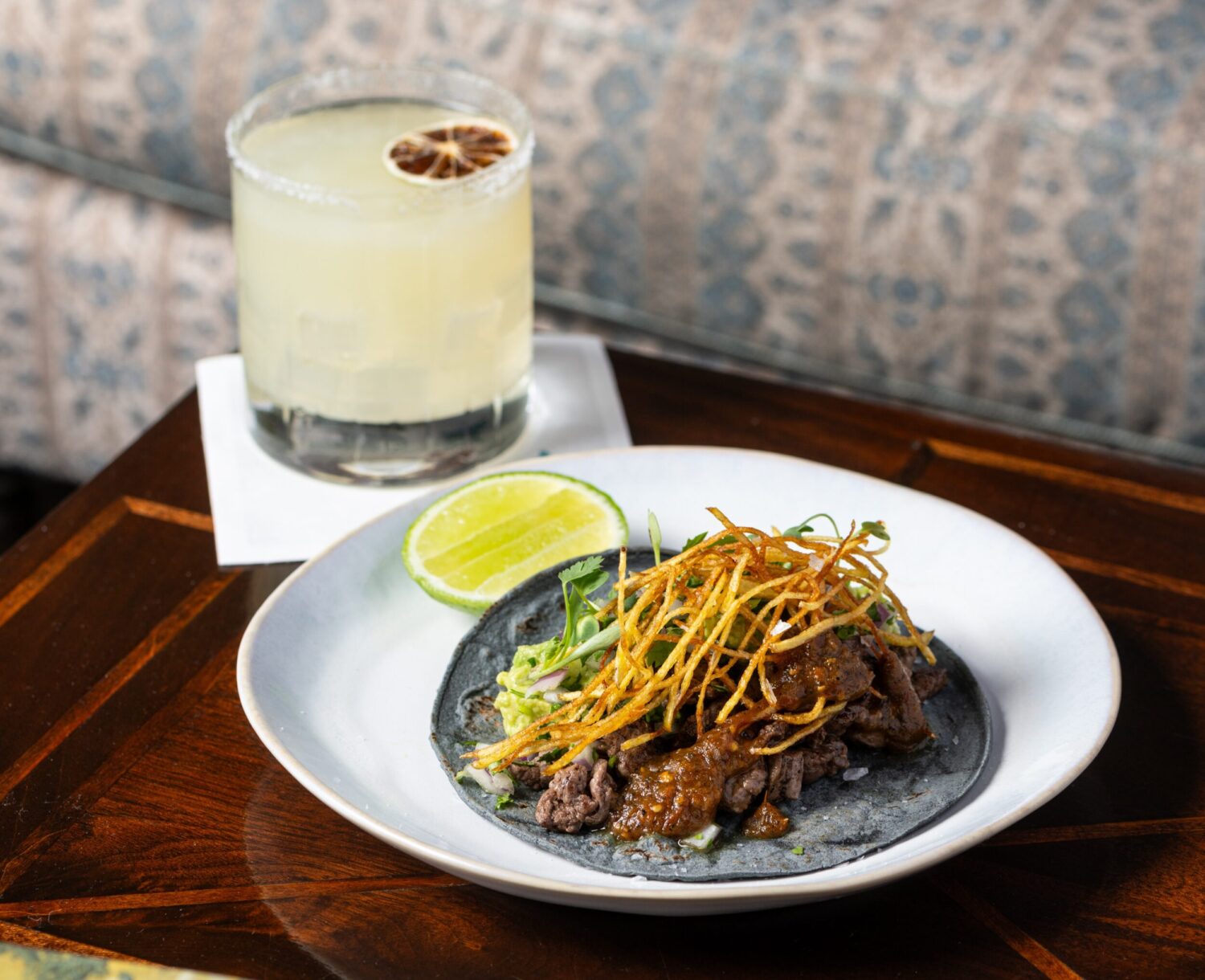 Plate of tacos with crispy onions and lime, paired with a cocktail in a salt-rimmed glass.