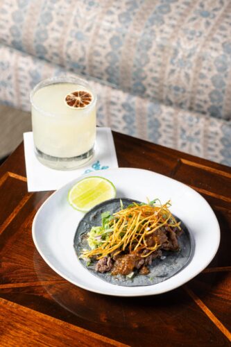 Plate of tacos with crispy onions and lime, paired with a cocktail in a salt-rimmed glass.