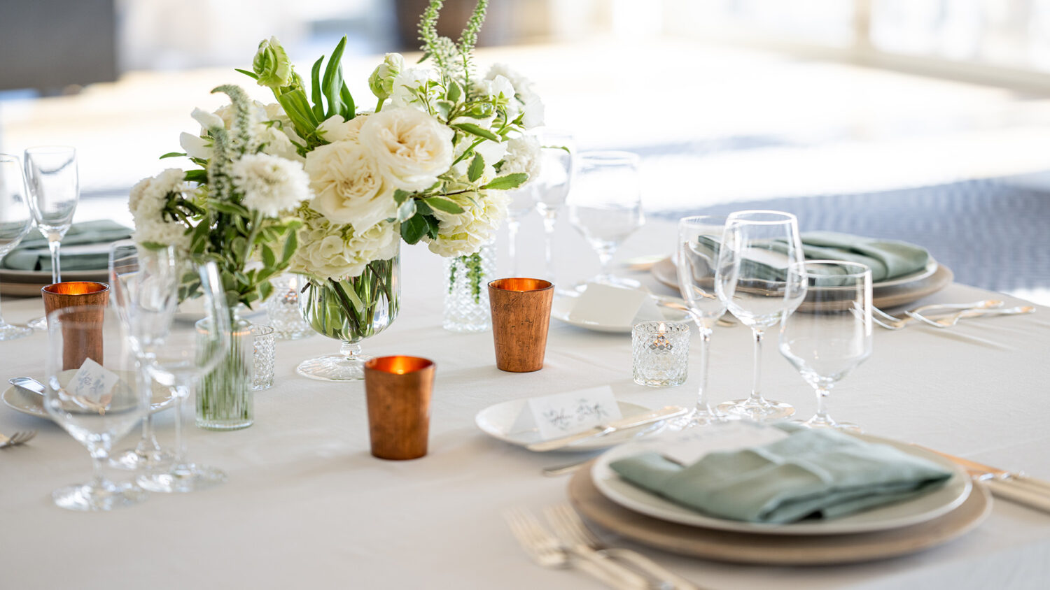 table setting with copper candles, white flowers and teal napkins