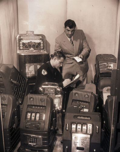 black & white photo of a police man and hotel staffer with slot machines