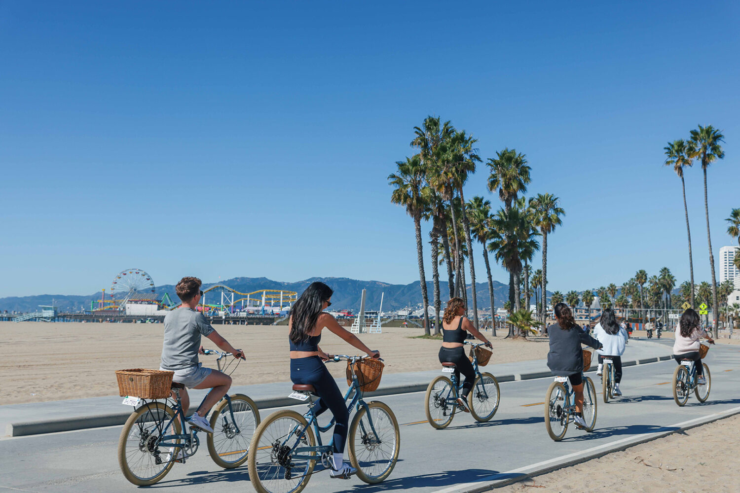 two woman in workout clothes, riding bikes on the boardwalk
