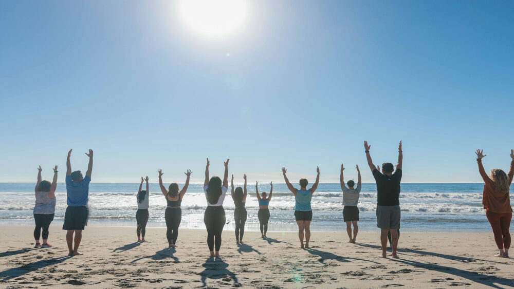 group of 10 people doing a yoga class on the beach