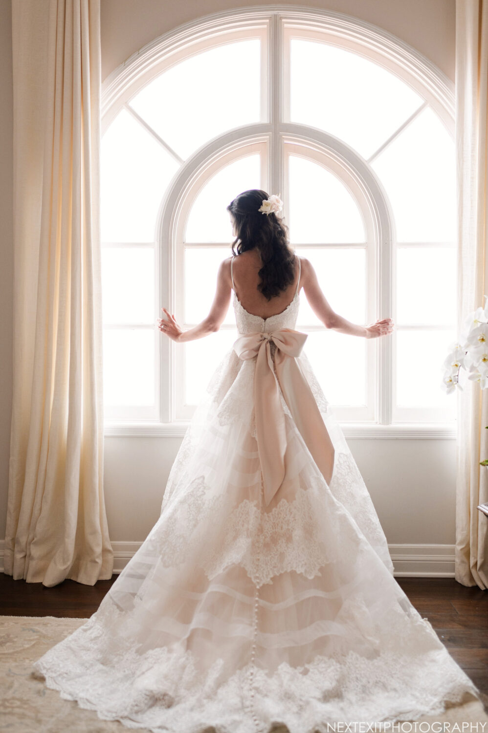 Bride in a white wedding dress with a bow, gazing out the window at a Santa Monica wedding venue.