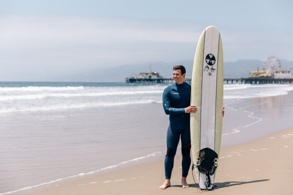 man in a wetsuit, holding a surf board looking out into the ocean
