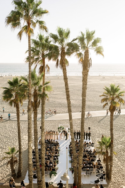 Beachfront wedding ceremony at Hotel Casa Del Mar, viewed through palm trees.