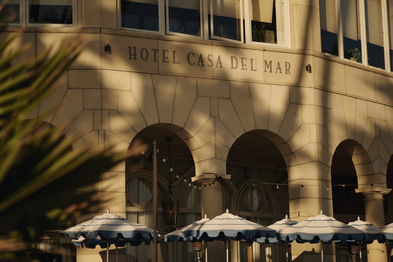 An exterior, close up shot of Casa del Mar Hotel with blue and white umbrellas and stringing lights