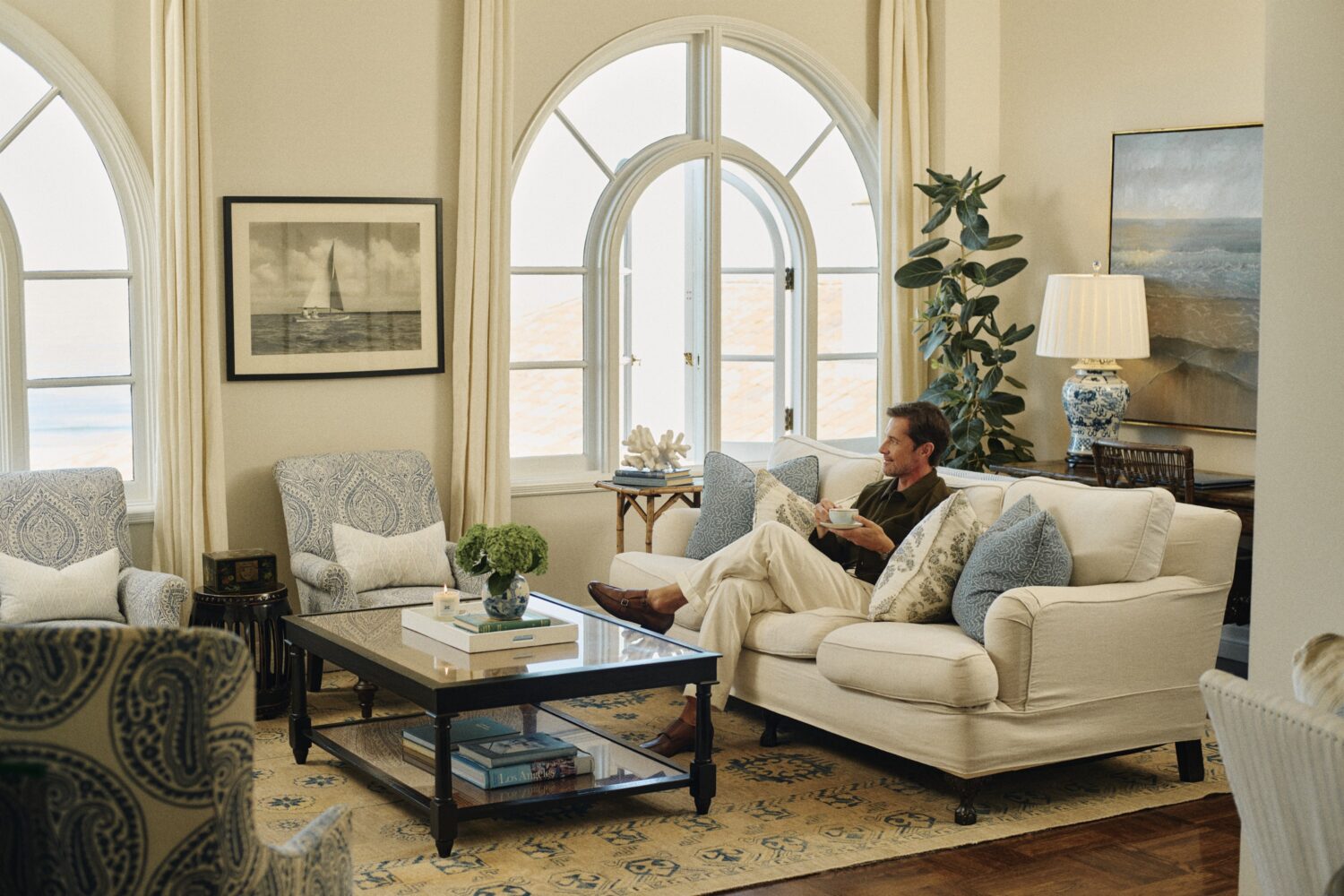 man sitting on the couch, holding a cup of tea, looking out the window, in the penthouse suite