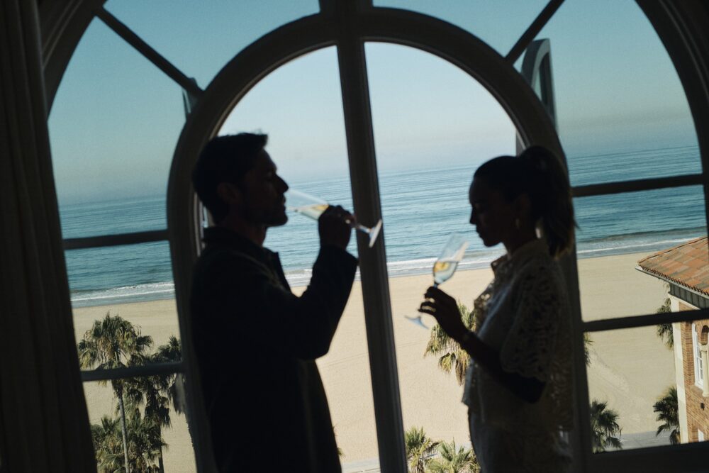 silhouette of a man and a woman sipping champagne by the window, with the ocean in the background