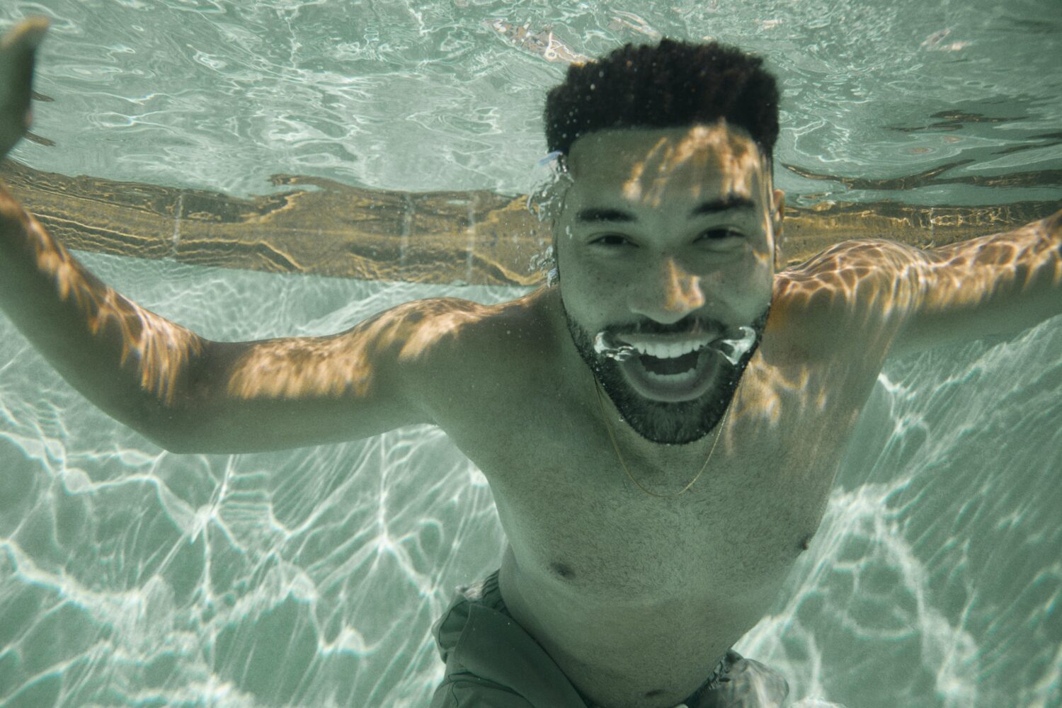 man smiling with his mouth open, underwater, in the pool