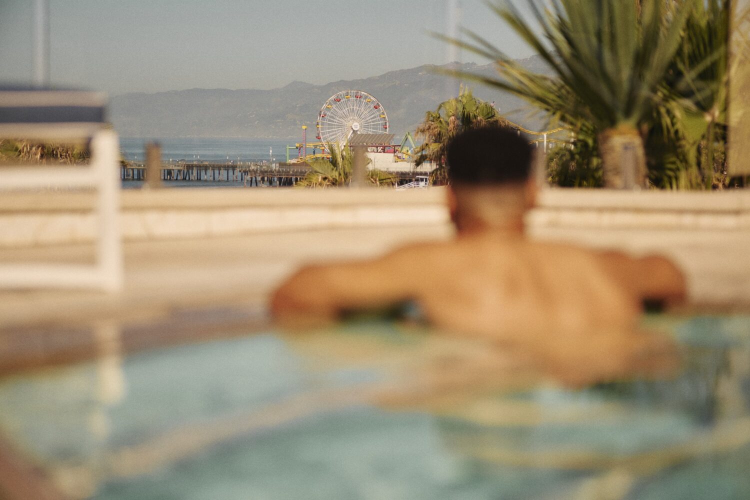 man in pool with a sharp focus on the Santa Monica Pier and Farris wheel