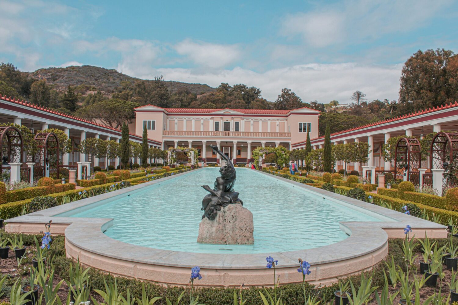 long fountain in a garden with a statue on a rock