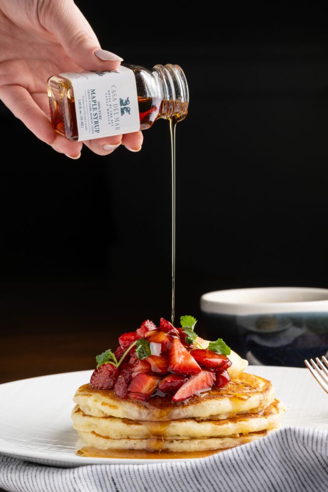 chef pouring casa del mar's signature maple syrup on a stack of pancakes with strawberries on top