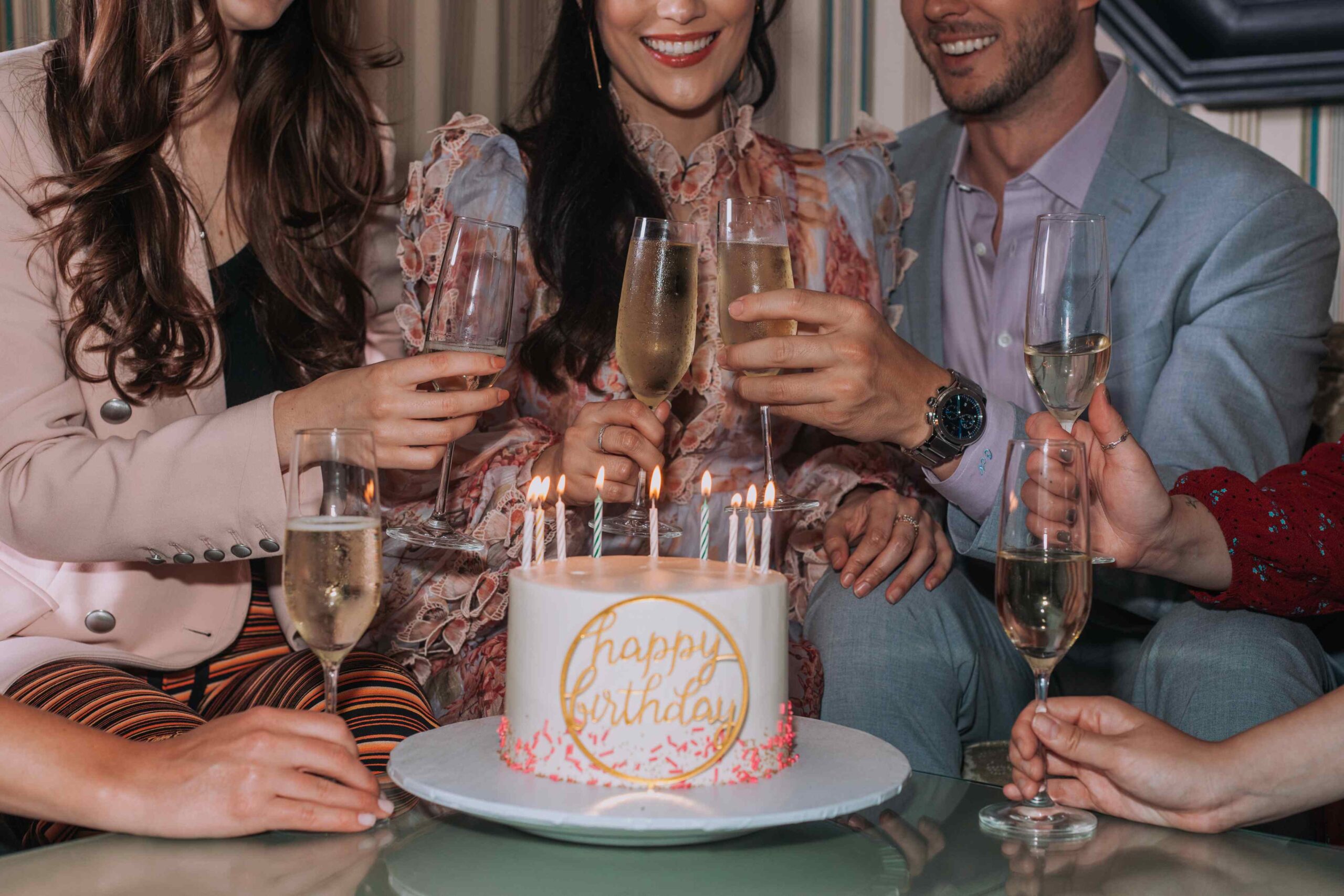 people around a birthday cake, clinking champagne glasses in celebration