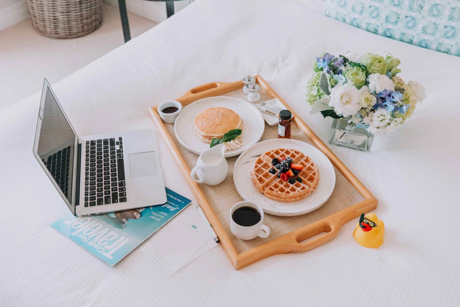 flowers, computer and room service on a platter on a bed