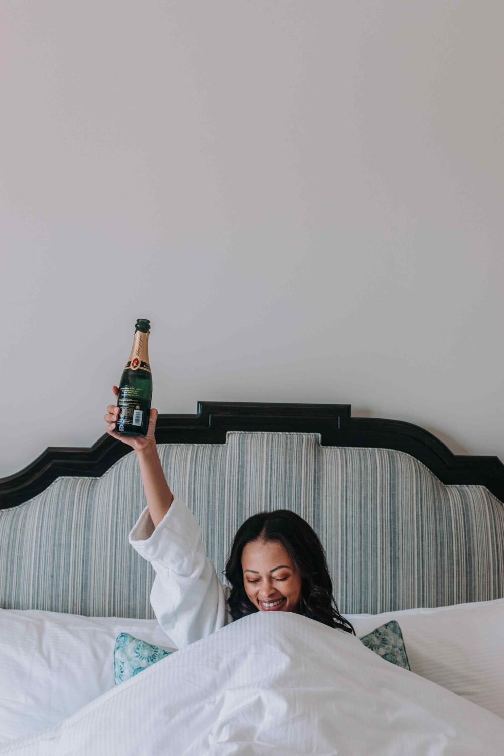woman in her bed with a bottle of champagne in the air