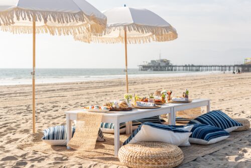 picnic setup on the beach with blue and white pillows and white umbrellas