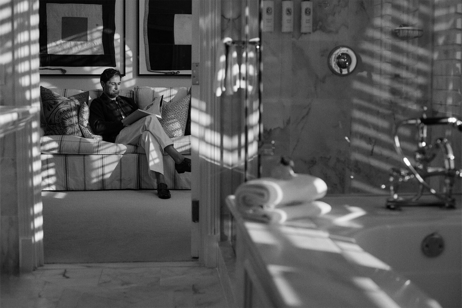 b&w image: man sitting on the couch, reading a coffee table book, in the penthouse suite