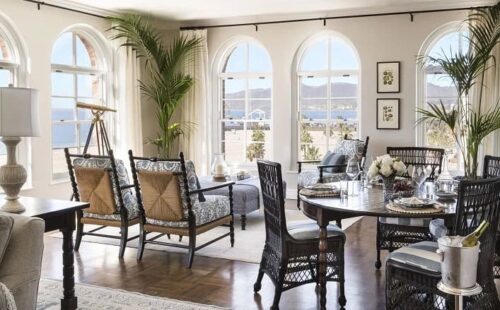 Sunlit living-dining space with arched windows, wicker furniture, and ocean views.